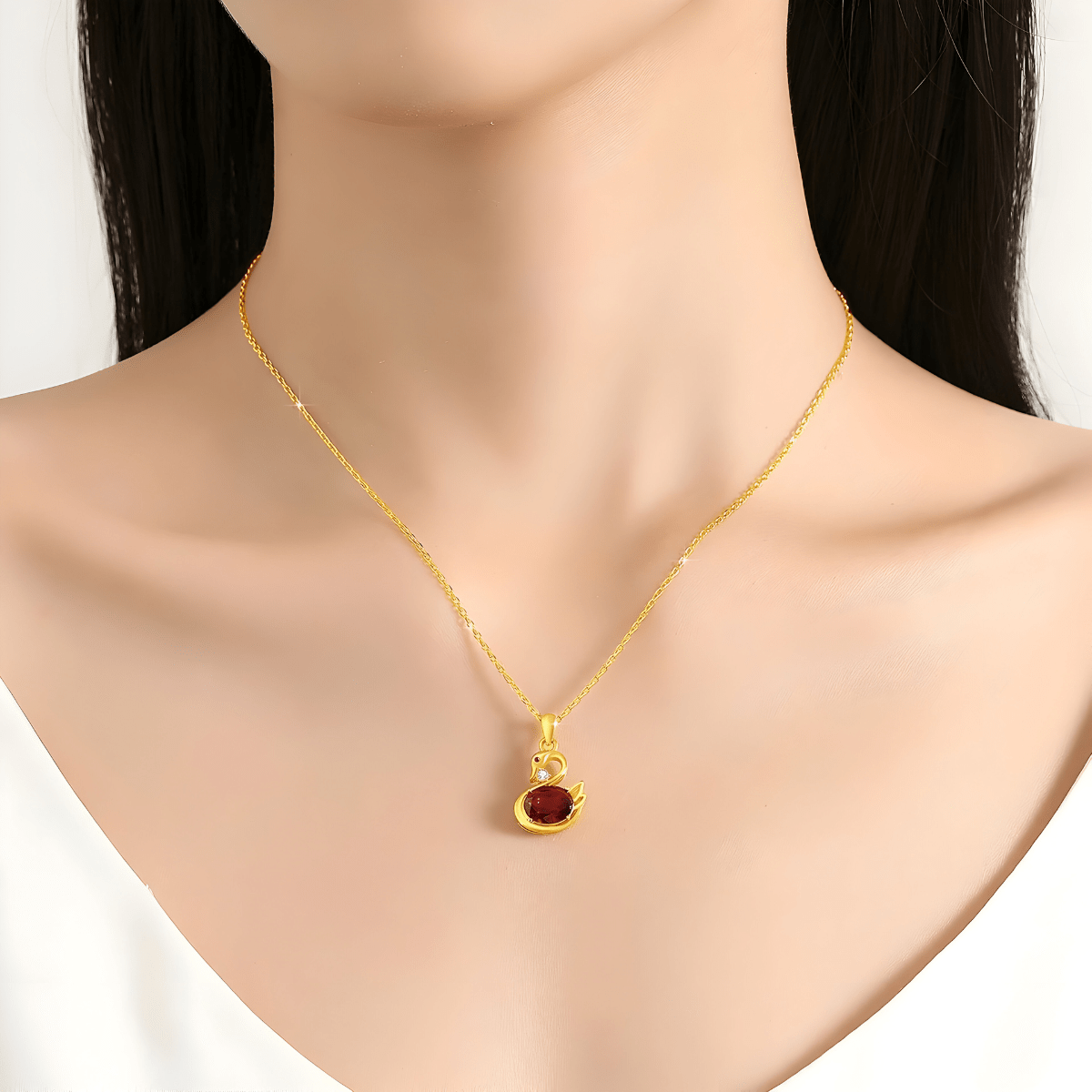 Collier grenat doré avec pendentif canard et pierre ovale rouge monté sur chaîne fine en métal doré, porté autour du cou d’une femme.