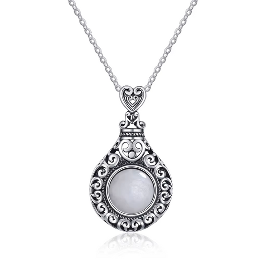 Un collier avec une pierre de lune blanche sertie dans un pendentif en argent finement orné de motifs en volutes élégantes.